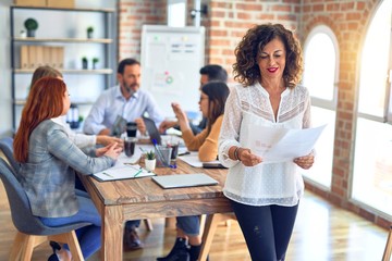 Group of business workers working together. Middle age beautiful businesswoman standing smiling happy looking at the camera at the office