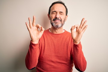 Middle age hoary man wearing casual orange sweater standing over isolated white background relaxed and smiling with eyes closed doing meditation gesture with fingers. Yoga concept.