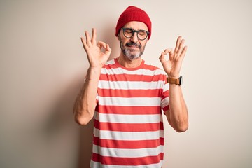 Naklejka premium Middle age hoary man wearing striped t-shirt glasses and cap over isolated white background relax and smiling with eyes closed doing meditation gesture with fingers. Yoga concept.