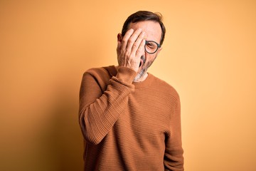 Middle age hoary man wearing brown sweater and glasses over isolated yellow background Yawning tired covering half face, eye and mouth with hand. Face hurts in pain.