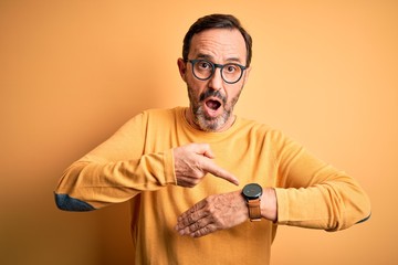 Middle age hoary man wearing casual sweater and glasses over isolated yellow background In hurry pointing to watch time, impatience, upset and angry for deadline delay