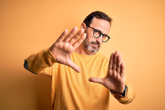 Middle age hoary man wearing casual sweater and glasses over isolated yellow background doing frame using hands palms and fingers, camera perspective