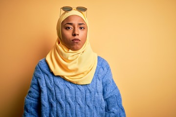 Young African American student woman wearing yellow muslim hijab and sunglasses with serious expression on face. Simple and natural looking at the camera.