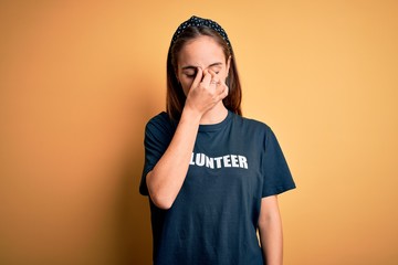 Young beautiful woman wearing volunteer t-shirt doing volunteering over yellow background tired...
