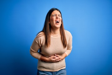 Young beautiful woman wearing casual sweater over blue background with hand on stomach because nausea, painful disease feeling unwell. Ache concept.