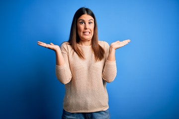 Young beautiful woman wearing casual sweater over blue background clueless and confused expression...