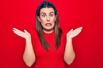 Young beautiful brunette woman wearing casual t-shirt standing over isolated red background...