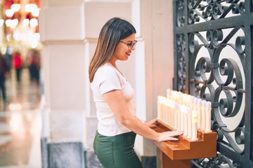 Young beautiful woman turning on candles at church