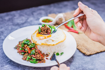 Hands using spoon the action of picking up rice topped with stir-fried beef and basil for eat, famous street food in Thailand, fast food, soft focus