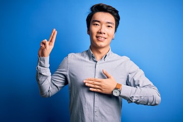 Young handsome chinese man wearing casual shirt standing over isolated blue background smiling...