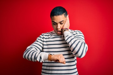 Young brazilian man wearing casual striped t-shirt standing over isolated red background Looking at...