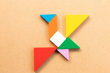 Color tangram puzzle in flying bird shape on wood bacground