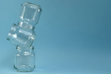 Vertical row of crooked glass jars on top of each other on a blue background, on the left closeup.