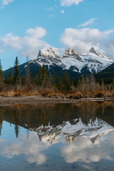 Breathtaking view of the iconic Three Sisters mountain peaks reflection in Policeman's Creek calm water while sunset. Canmore, Alberta, Canada.