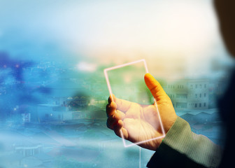 A transparent smart phone is being seen by a businessman against a skyscraper city covered in cold fog.