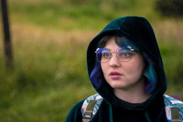 Portrait of a colored hair woman with eyeglasses and a dark green hoodie looking aside with a surprise expression. 