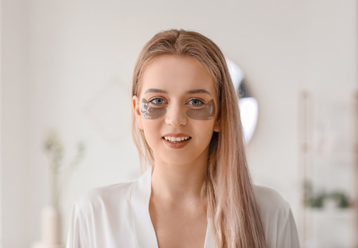 Beautiful young woman with under-eye patches in bathroom