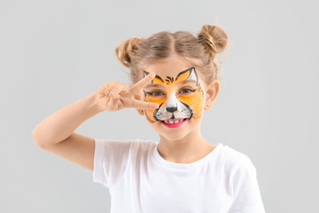 Funny little girl with face painting on light background