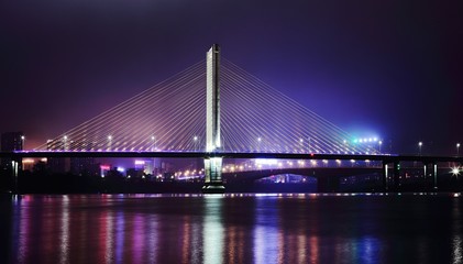 Fototapeta na wymiar Suspension Bridge With City Lit Up At Night