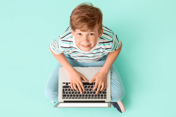 Cute little boy with laptop on color background. Concept of online education