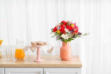 Vase with bouquet of beautiful flowers on table in kitchen