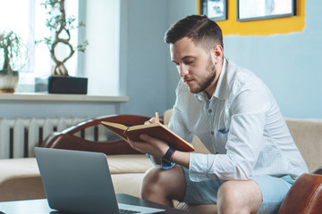 Young freelancer writing down in a notebook while working from home