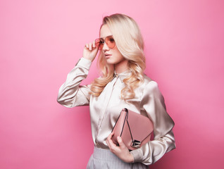 Beautiful young blond woman in a blouse wearing glasses, holding handbag.