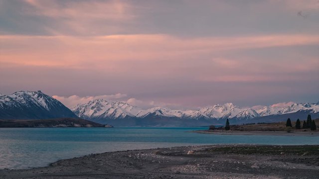Late afternoon sunset over blue Lake Tekapo with clouds moving over snow covered mountain peaks in the background. 4k time lapse captured in the South Island of New Zealand