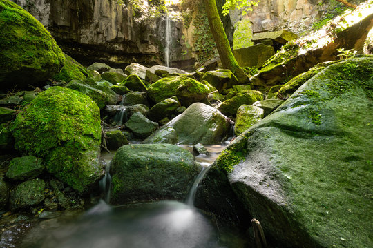 Wide angle view of a mountain waterfall, with its stream of water rushing between moss-covered rocks and into a small pond