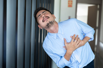 Young Businessman holding his heart in pain while in workplace.