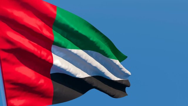 The national flag of UAE flutters in the wind against a blue sky