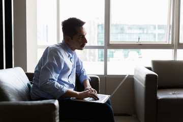 A young businessman using laptop working with happy on sofa in modern office.