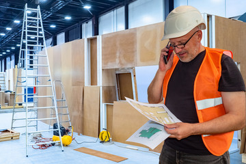 Builder by phone and drawings in the hands. Builder prepares a temporary room. Builder is studying the plan of the exhibition pavilion. Engineer talking on the phone. Concept - event organization