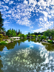 Obraz premium April 2019, California: Beautiful cloud reflections off the lake water in landscaped gardens with beautiful flowers, bushes, trees, bridges and buildings in southern California 