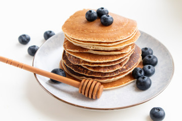 Delicious pancakes with fresh blueberries and honey dipper on plate