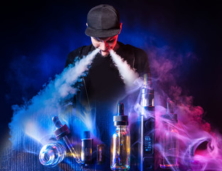 Vaping. VAPE shop. Smoking electronic cigarettes. The man lets out two streams of smoke from the VAPE. Smoker on the background of VAPE devices.