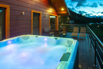 Evening in the cottage village. A hot tub with lighting on the house's terrace. Water treatments in...