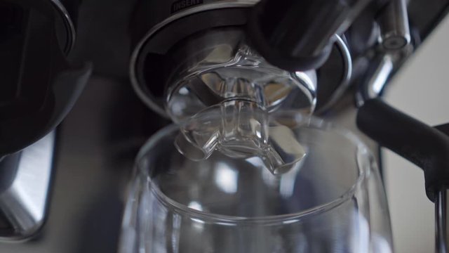 Close up of espresso coffee machine portafilter brewing extracting double shot into glass 