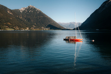 Red boat tied to a buoy in lake Achensee surrounded by mountains in the Austrian Alps.