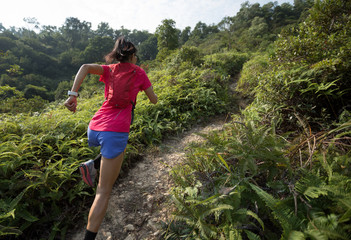 Woman trail runner running up on mountain slope in tropical forest