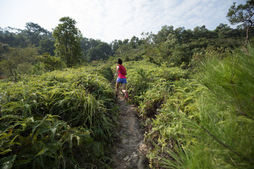 Woman trail runner running up on mountain slope in tropical forest