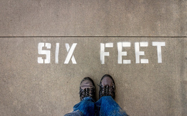 Looking down on sign stenciled in white capital letters stating SIX FEET to indicate social...