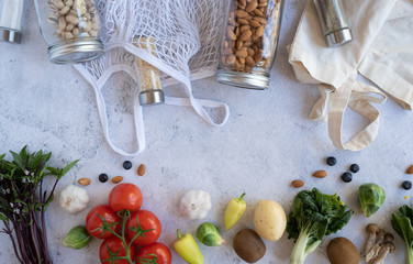 zero waste lifestyle .cotton net bag with fresh vegetables and sustainable glass jar on cement background flat lay.plastic free for groceries product shopping and delivery. food and healthy diet.