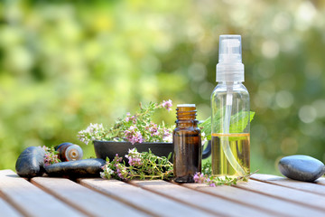 bottles of essential oil and flowers of aromatic herb on atable and on green background
