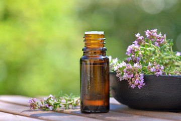 bottle of essential oil and flowers of aromatic herb on a table on green background