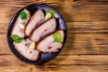 Slices of baked pork belly, garlic and parsley on a black plate. Top view