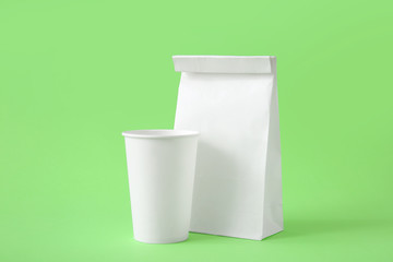 Paper bag and cup on color background