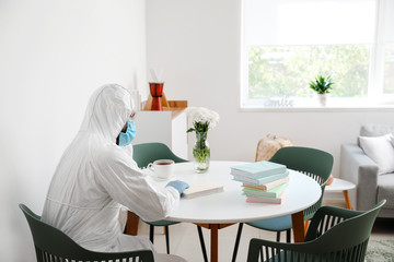Man in biohazard suit and with books at home