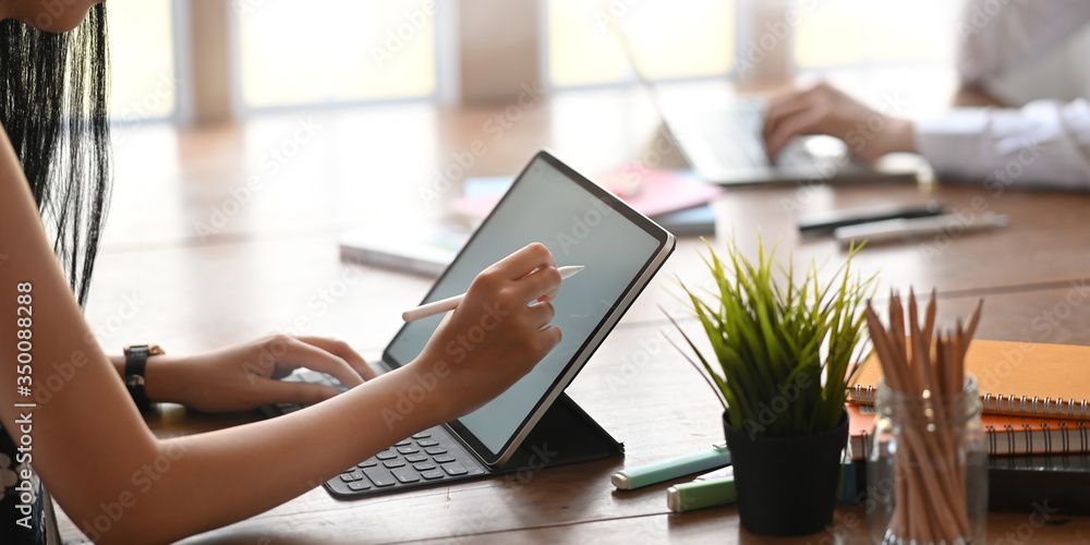 Poster cropped image of graphic designer writing/sketching on white blank screen computer tablet by using a