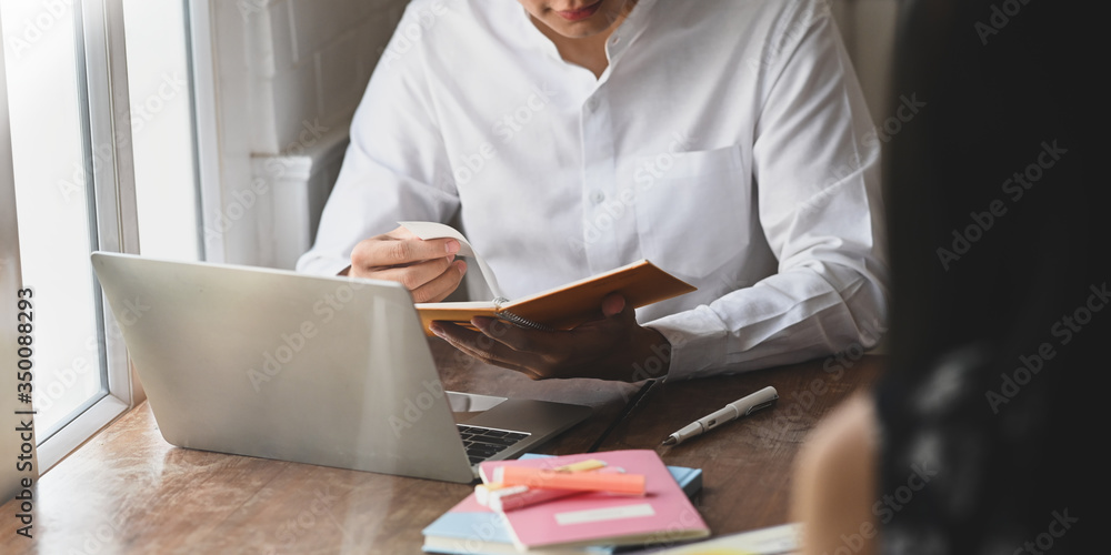 Poster cropped image of businessman taking notes while sitting in front of computer laptop and his colleagu